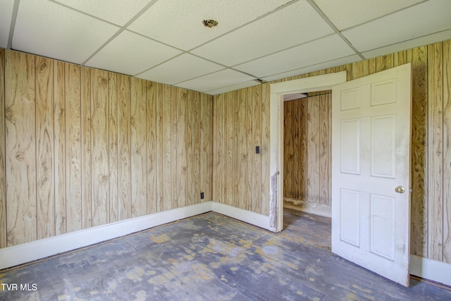 spare room with wooden walls, concrete floors, baseboards, and a paneled ceiling