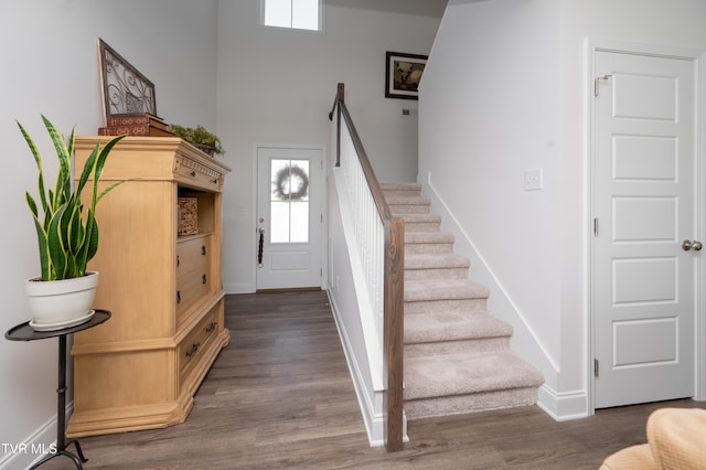 staircase with wood finished floors, a towering ceiling, and baseboards