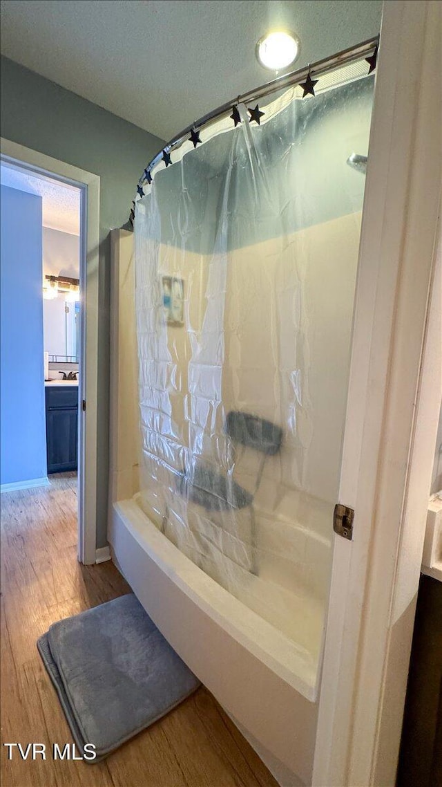 bathroom with a textured ceiling, vanity, wood finished floors, shower / tub combo with curtain, and baseboards
