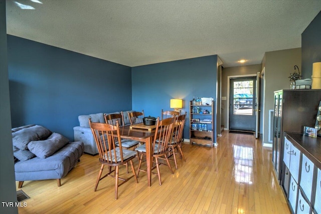 dining area featuring light wood finished floors, a textured ceiling, and baseboards