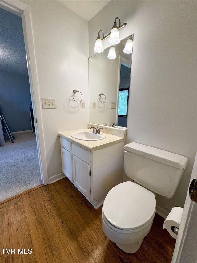 half bathroom featuring toilet, wood finished floors, vanity, and baseboards