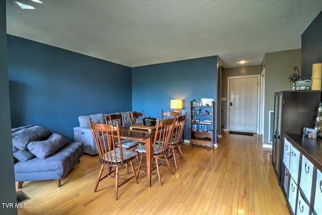 dining room featuring a textured ceiling, baseboards, and light wood-type flooring