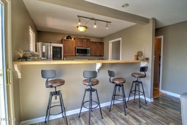 kitchen featuring baseboards, a kitchen bar, brown cabinetry, stainless steel appliances, and wood finished floors