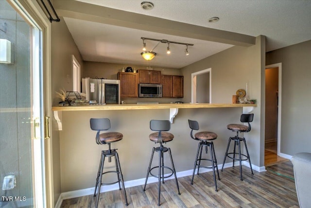 kitchen featuring brown cabinets, appliances with stainless steel finishes, wood finished floors, and a breakfast bar area