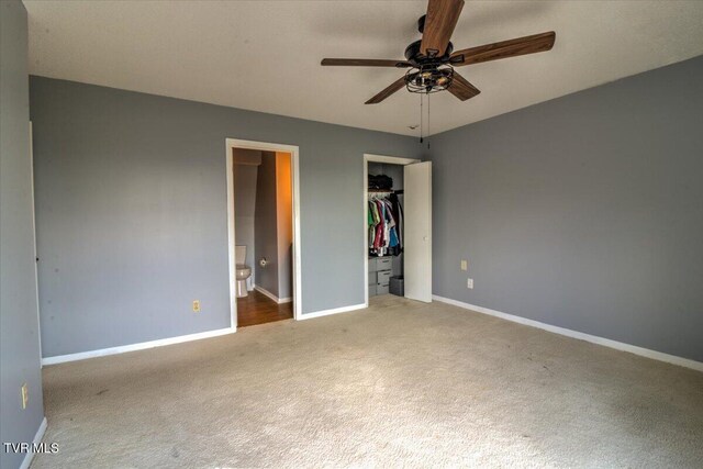 unfurnished bedroom with a closet, baseboards, a ceiling fan, carpet, and ensuite bath