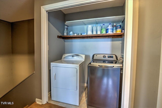 clothes washing area featuring light wood-style flooring, washer and clothes dryer, and baseboards