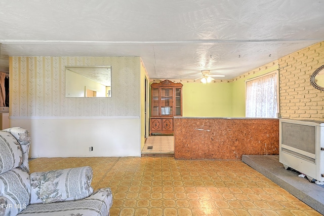living room with wallpapered walls, heating unit, a ceiling fan, and a wainscoted wall