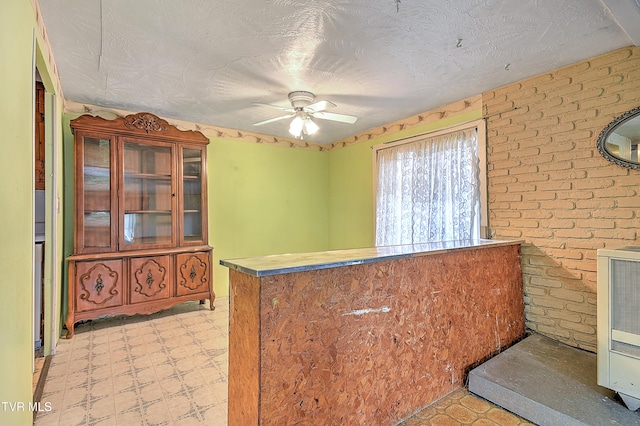 interior space with brick wall, ceiling fan, light floors, and a textured ceiling