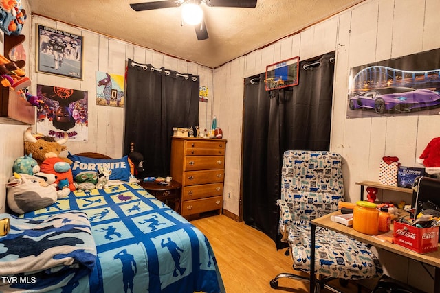bedroom with a textured ceiling, wood finished floors, wooden walls, and a ceiling fan