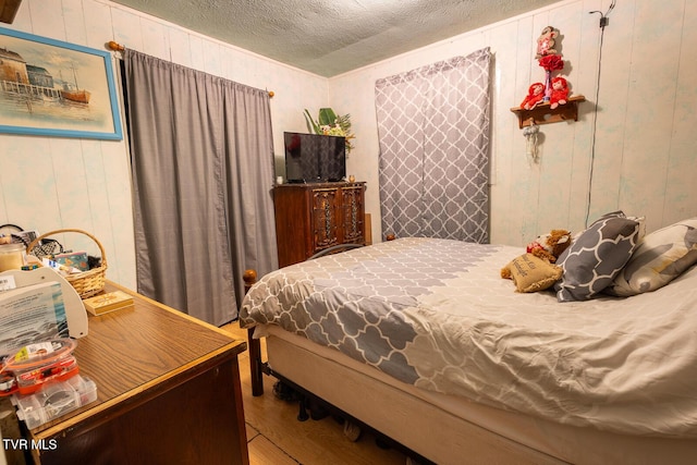 bedroom with a textured ceiling, wood finished floors, and wood walls
