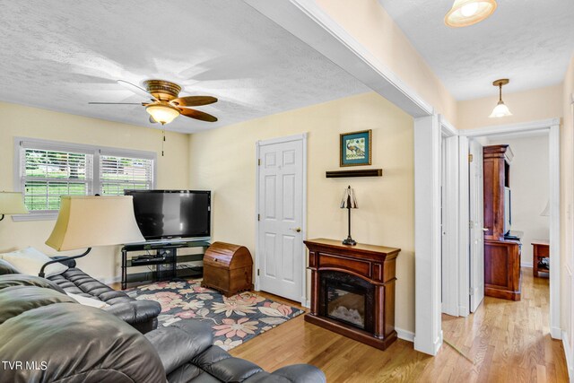 living room featuring baseboards, a textured ceiling, wood finished floors, and ceiling fan