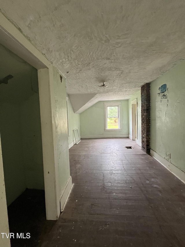 additional living space featuring visible vents, baseboards, a textured ceiling, wood finished floors, and lofted ceiling