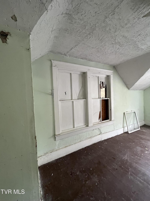 additional living space featuring baseboards, vaulted ceiling, and a textured ceiling