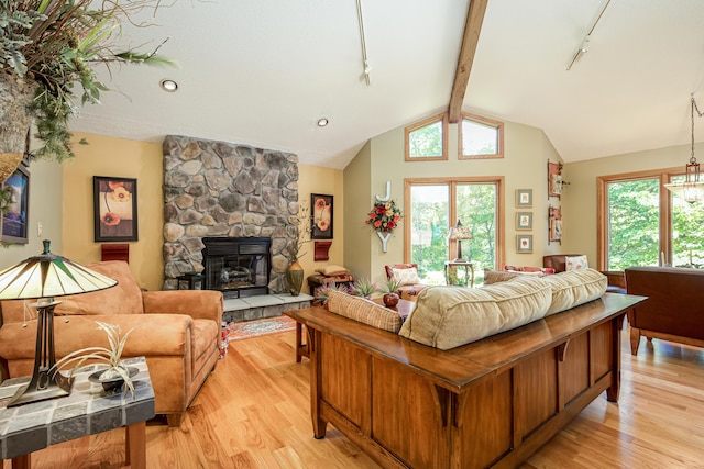 living room featuring track lighting, a stone fireplace, light wood-style floors, and lofted ceiling with beams
