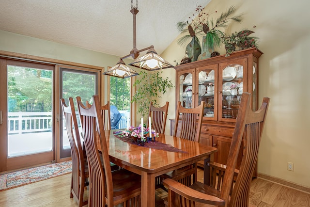 dining room featuring light wood-style flooring, a textured ceiling, baseboards, and vaulted ceiling