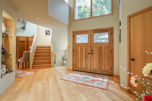 foyer with stairs, a towering ceiling, baseboards, and wood finished floors