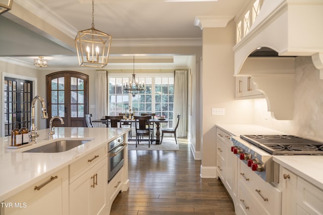 kitchen featuring a sink, hanging light fixtures, stainless steel appliances, custom range hood, and a notable chandelier