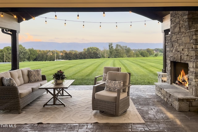 patio terrace at dusk featuring an outdoor living space with a fireplace, a mountain view, and a lawn
