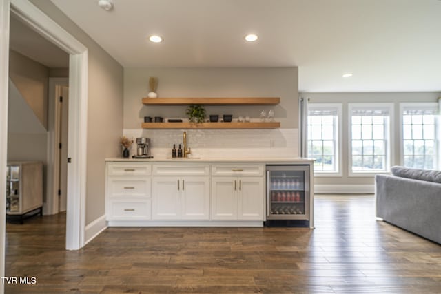 bar featuring dark wood-type flooring, tasteful backsplash, wet bar, a sink, and beverage cooler