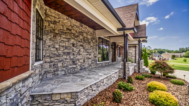 view of side of property featuring roof with shingles and stone siding