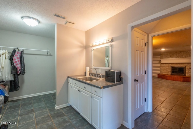 full bathroom with a glass covered fireplace, vanity, baseboards, a textured ceiling, and visible vents