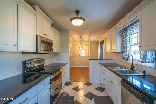 kitchen with light tile patterned floors, white cabinetry, dark countertops, appliances with stainless steel finishes, and a sink