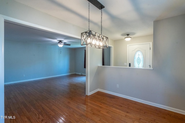 empty room featuring baseboards, ceiling fan with notable chandelier, and dark wood finished floors