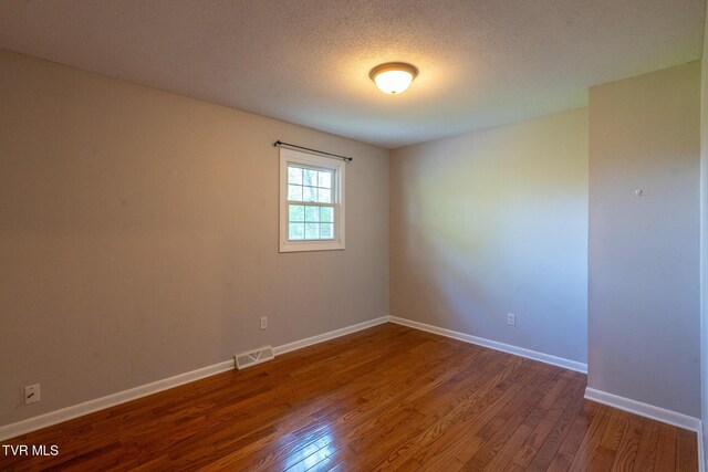 empty room featuring visible vents, baseboards, a textured ceiling, and wood finished floors