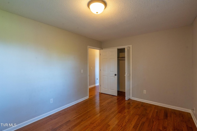 unfurnished bedroom with a closet, baseboards, wood finished floors, and a textured ceiling