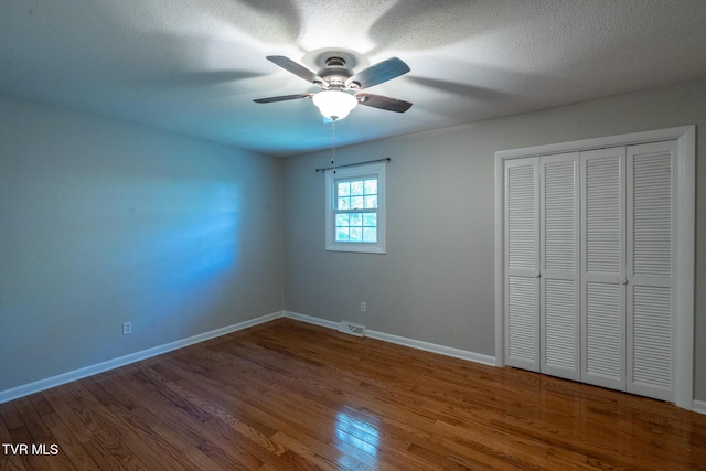 unfurnished bedroom with ceiling fan, a closet, visible vents, wood finished floors, and baseboards