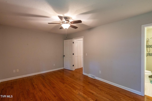 empty room with wood finished floors, baseboards, a ceiling fan, and visible vents