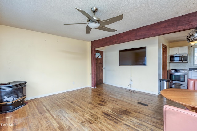 living room featuring visible vents, a wood stove, a ceiling fan, light wood-style floors, and a textured ceiling