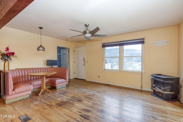 living area with visible vents, a wood stove, a ceiling fan, and wood finished floors