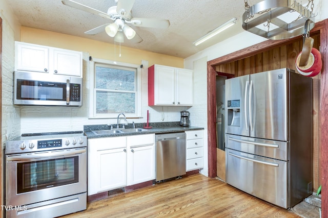 kitchen featuring a textured ceiling, white cabinetry, appliances with stainless steel finishes, a sink, and dark countertops
