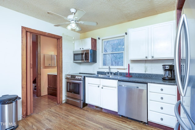 kitchen with light wood-type flooring, white cabinets, dark countertops, a sink, and stainless steel appliances