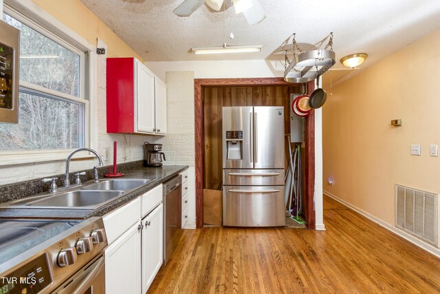 kitchen with visible vents, white cabinets, a sink, appliances with stainless steel finishes, and light wood finished floors