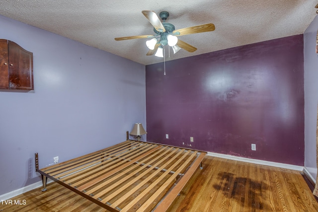 empty room featuring ceiling fan, baseboards, wood finished floors, and a textured ceiling