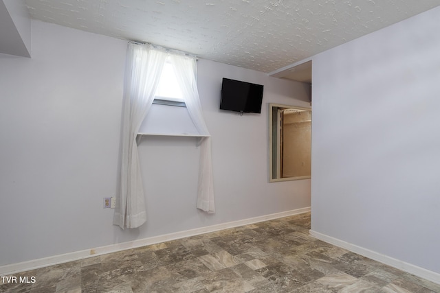 spare room with baseboards, a textured ceiling, and stone finish flooring