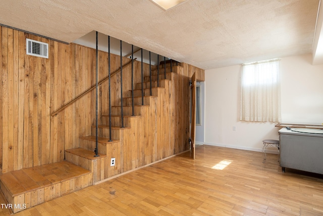 basement featuring baseboards, a textured ceiling, wood walls, stairs, and visible vents