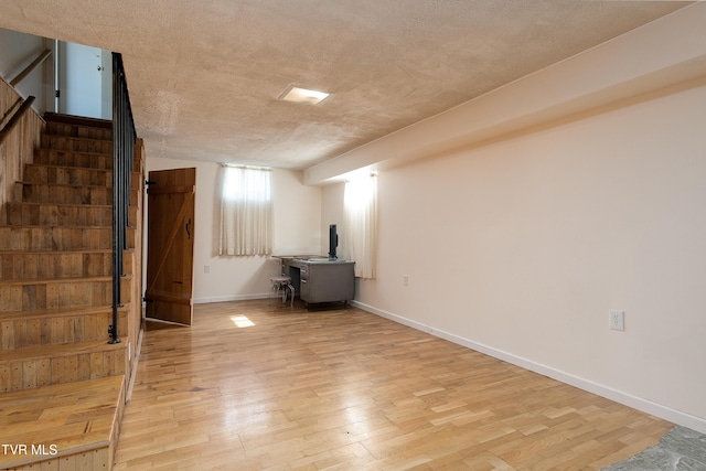 below grade area featuring a textured ceiling, light wood finished floors, baseboards, and stairs