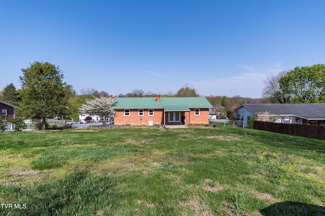 rear view of property featuring metal roof, fence, and a lawn