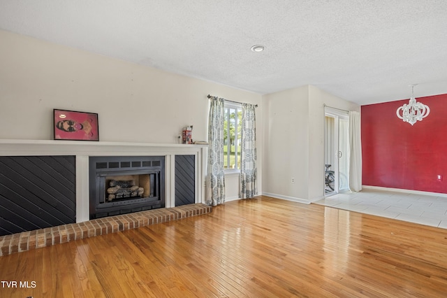 1023 Pebble Dr, Bristol, VA 24201 - unfurnished living room featuring baseboards, an inviting chandelier, a fireplace, a textured ceiling, and wood finished floors