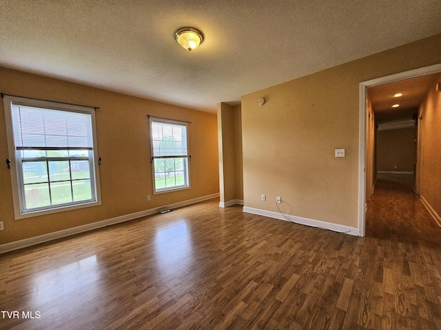 unfurnished room featuring a textured ceiling, dark wood-style flooring, and baseboards