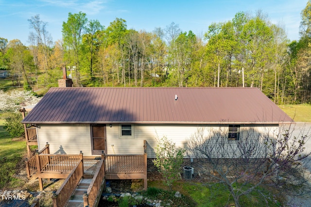 rear view of house with metal roof, a wooden deck, a chimney, and cooling unit