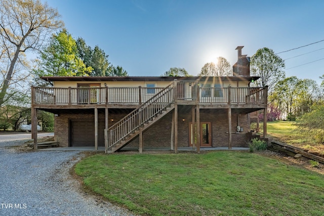 back of house featuring a deck, a yard, a chimney, brick siding, and gravel driveway