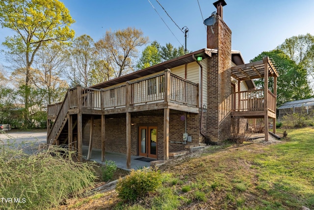 rear view of house featuring brick siding, french doors, a deck, and a chimney