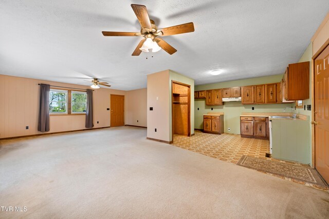 kitchen with ceiling fan, under cabinet range hood, a sink, brown cabinets, and baseboards