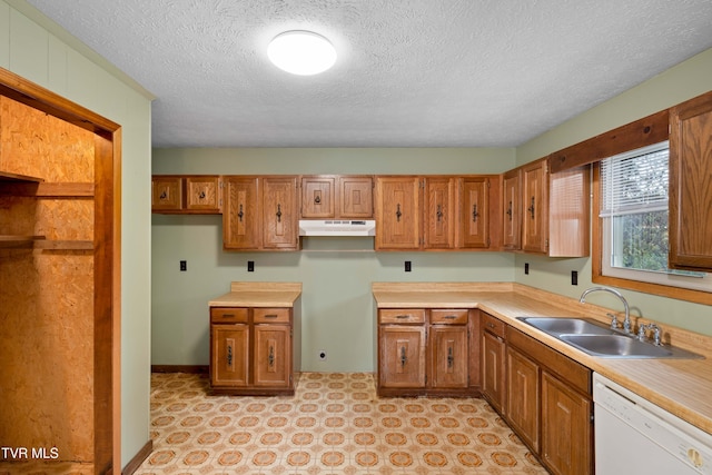 kitchen with brown cabinetry, a textured ceiling, under cabinet range hood, a sink, and white dishwasher