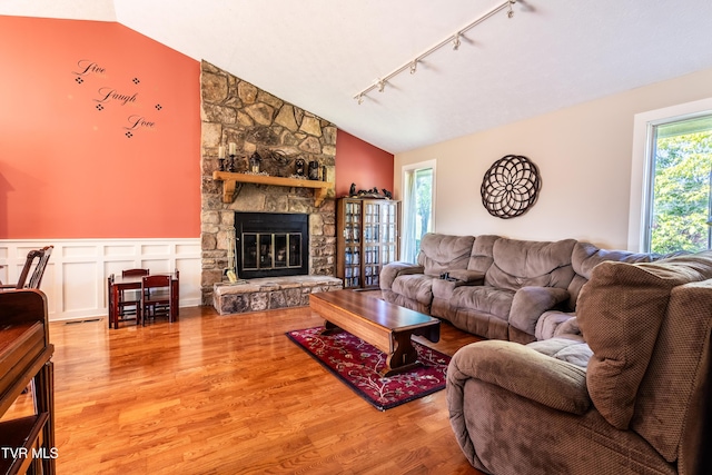 living area featuring track lighting, lofted ceiling, wood finished floors, a fireplace, and a wainscoted wall