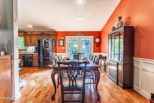 dining space featuring wine cooler, a wainscoted wall, plenty of natural light, light wood-type flooring, and a textured ceiling